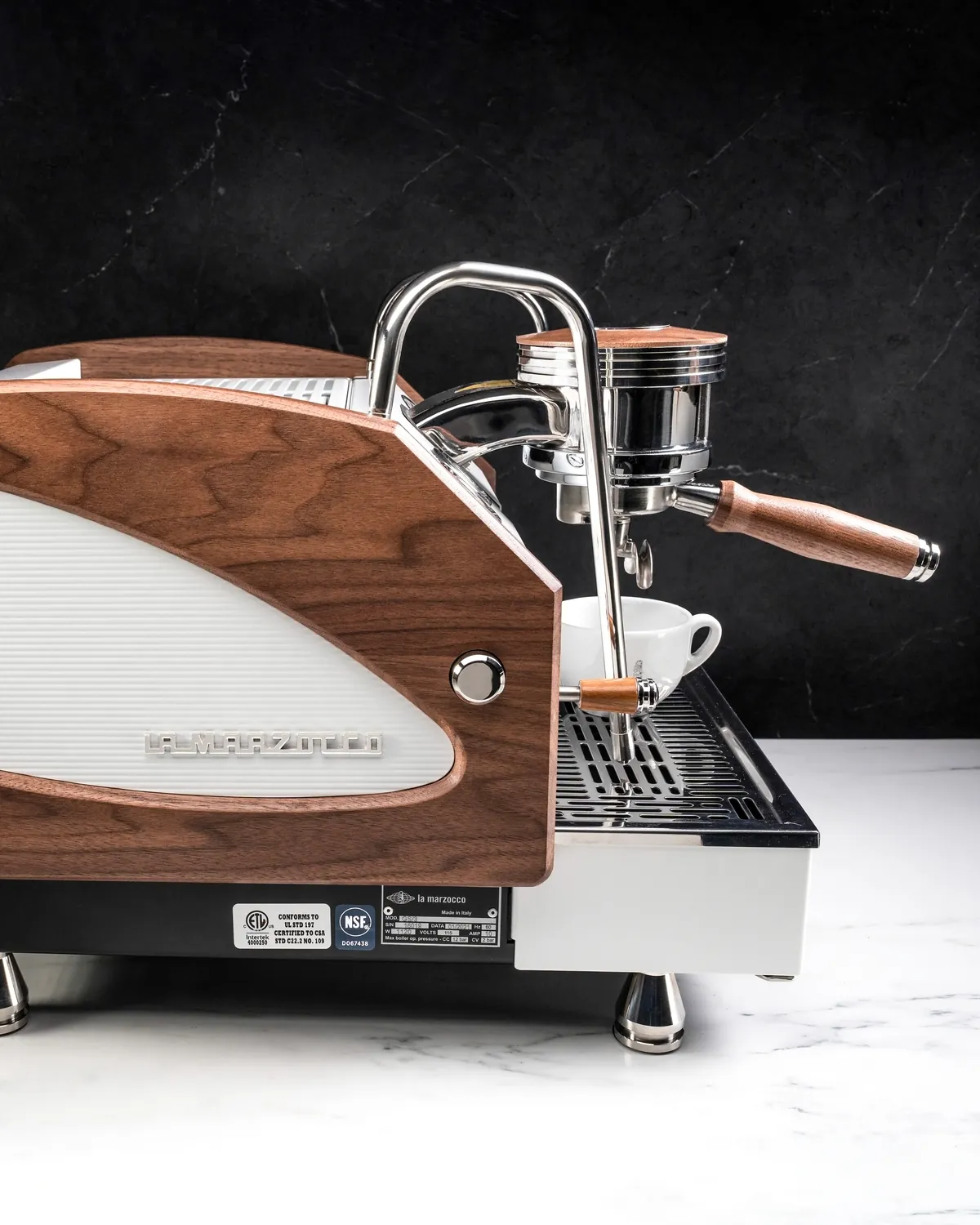 Walnut-clad espresso machine with a chrome group head, wooden portafilter and a white cup