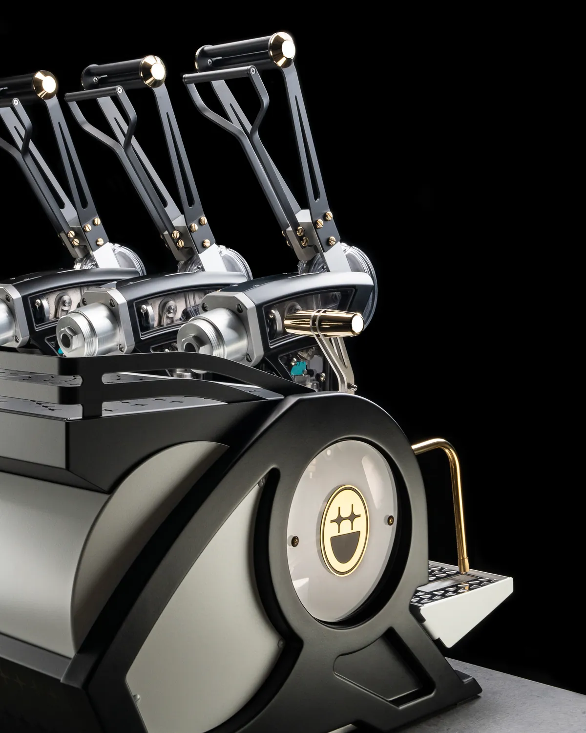 Three-group lever espresso machine in black and grey with brass and chrome accents