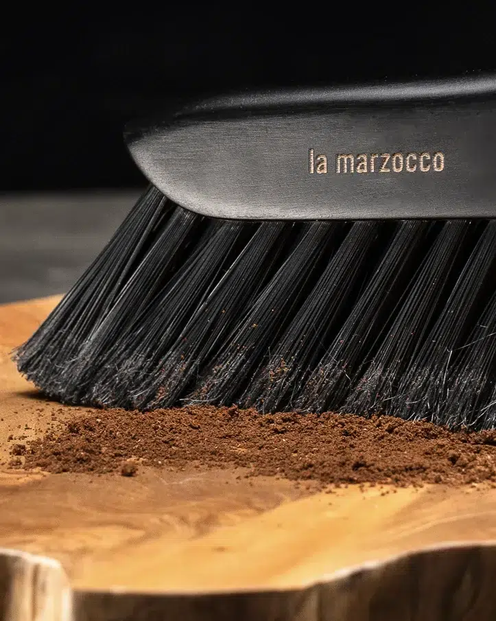 La Marzocco barista brush sweeping ground coffee across a live-edge wooden board
