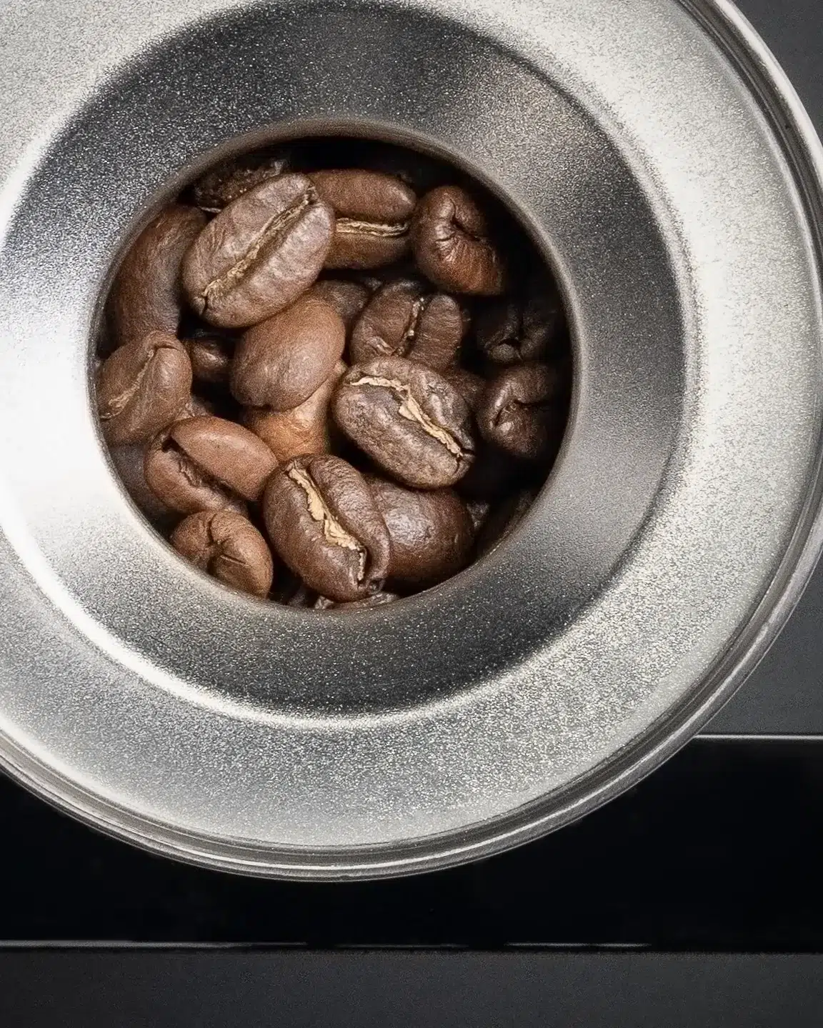 Roasted coffee beans in a stainless steel La Marzocco dosing cup, seen from above