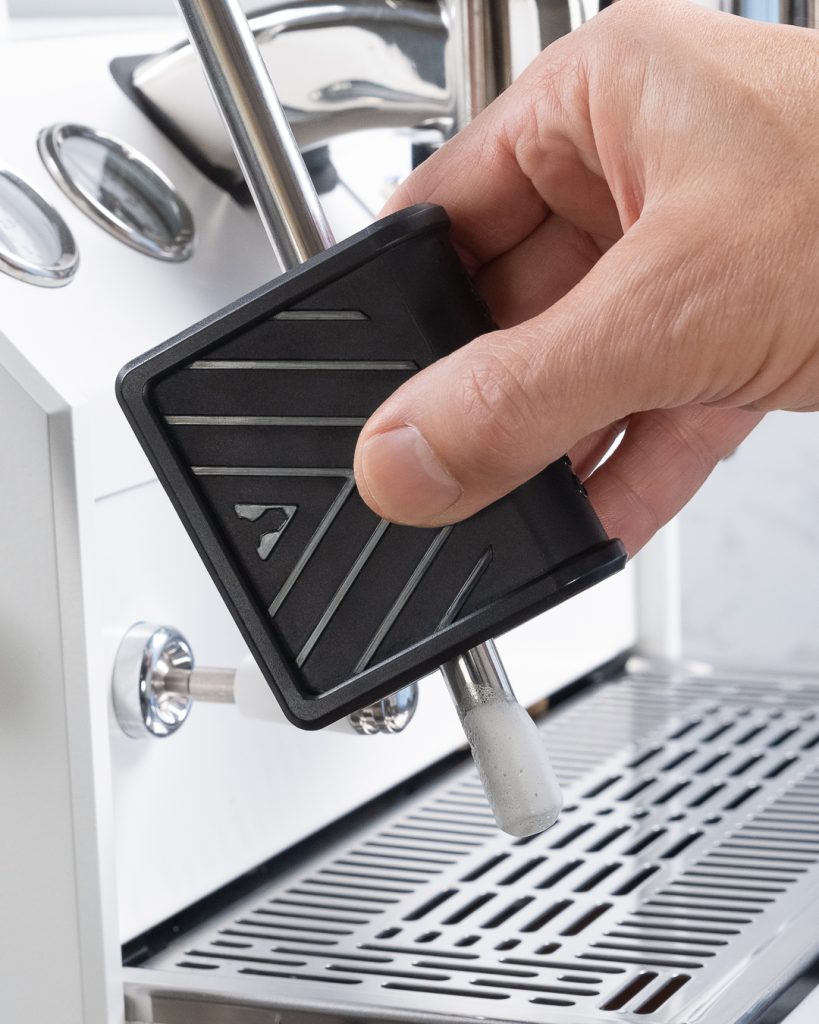 Hand closing the steam wand cleaning tool around the tip of a white espresso machine's steam wand