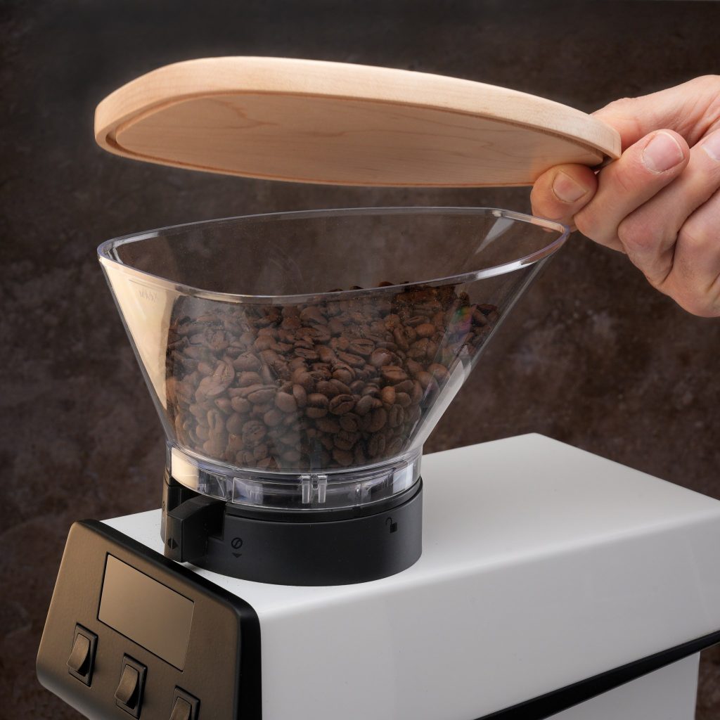 Hand lifting the Artpresso maple hopper lid clear of the La Marzocco Pico grinder hopper to top up the beans