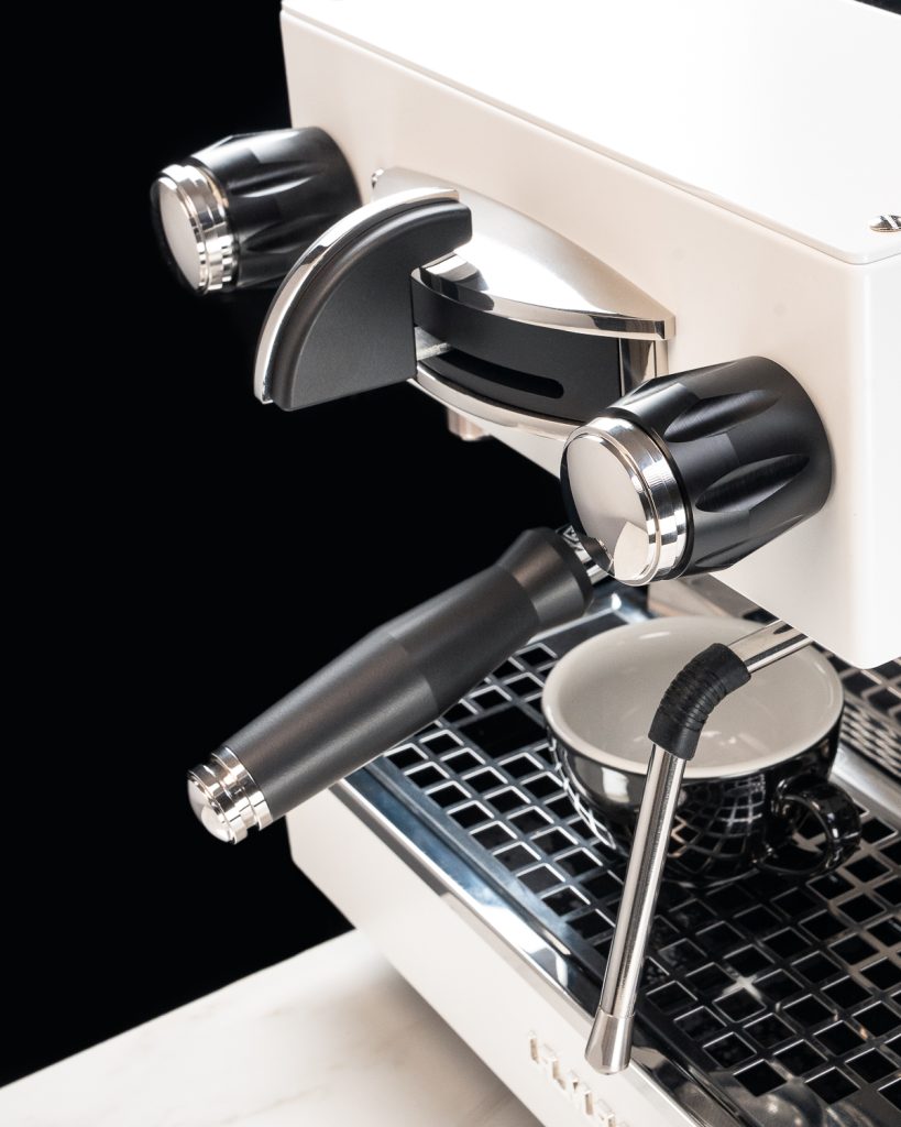 Black steam knob, brew paddle and portafilter handle fitted to a white La Marzocco Linea Mini against a black background
