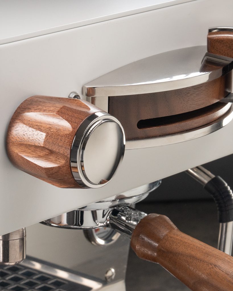 Close detail of a walnut steam knob and walnut brew paddle on a white La Marzocco Linea Mini, with the walnut portafilter handle below