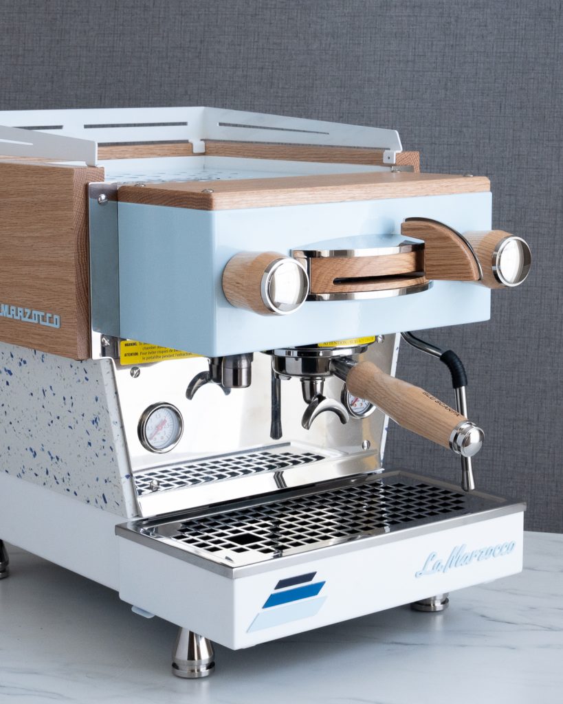 La Marzocco Linea Mini with a pale blue front panel, walnut top rail and side trim, a speckled lower panel and a walnut portafilter handle, on white marble