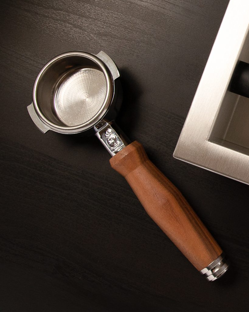 Portafilter with a walnut handle and a fitted basket resting on a dark counter