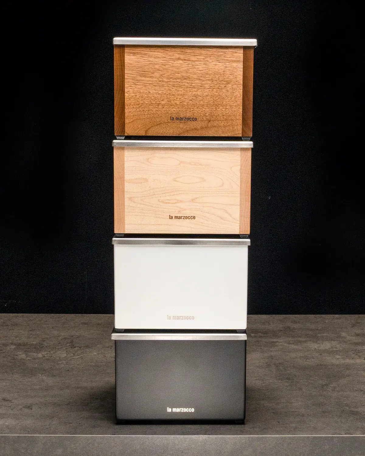 Four stacked La Marzocco storage boxes in walnut, oak, white and graphite finishes