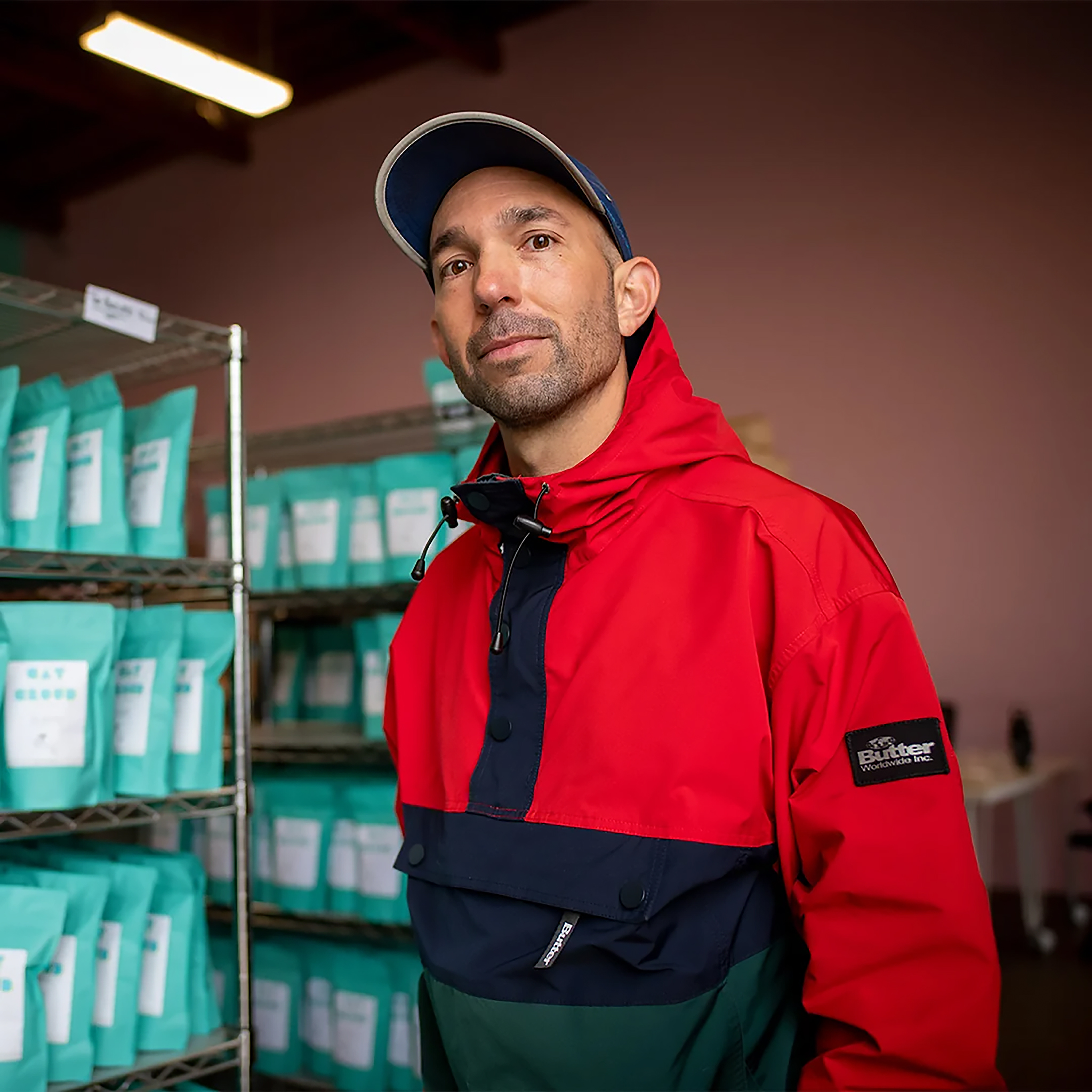 Chris Baca in a red and navy jacket beside shelves of teal coffee bags