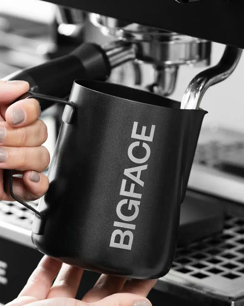 Black BIGFACE milk pitcher held at the espresso machine