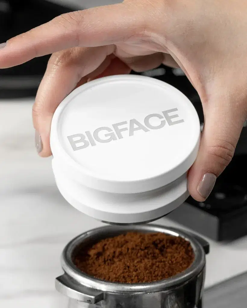 White BIGFACE coffee distributor held above a portafilter of ground coffee