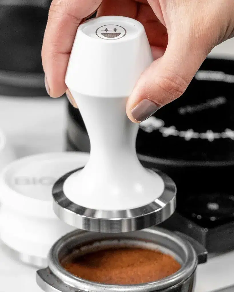 White BIGFACE espresso tamper being lowered onto a portafilter of ground coffee