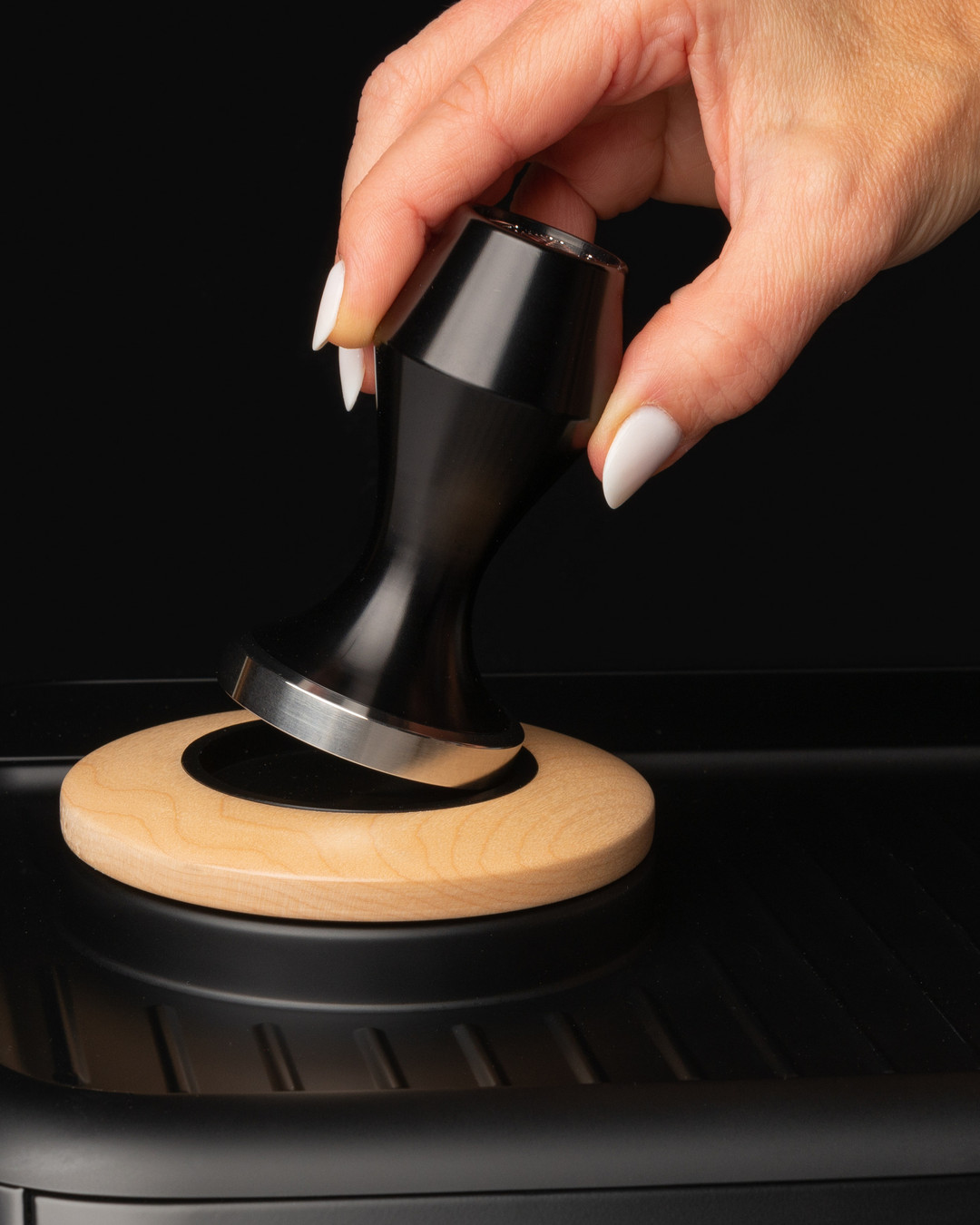 Hand lowering a black Artpresso tamper onto a maple tamper holder set into the top of a Breville espresso machine