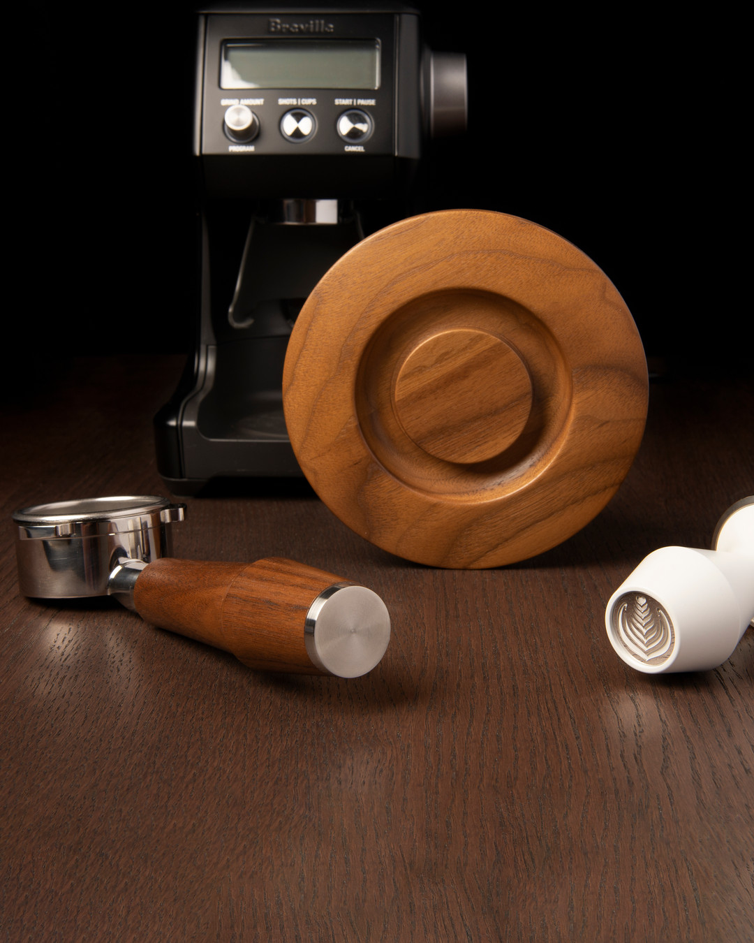 Walnut Artpresso tamper holder with a walnut handled portafilter and a white tamper on a dark wood counter in front of a Breville grinder