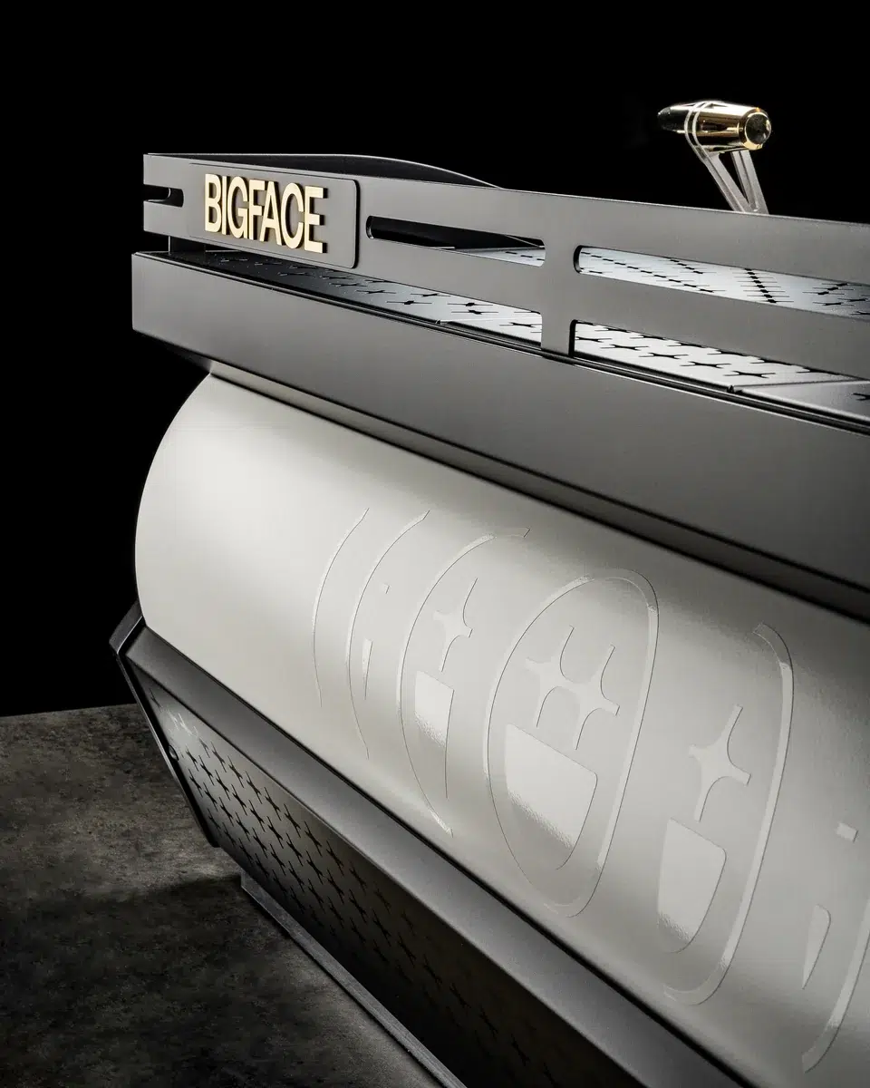 Gold BIGFACE nameplate on the top rail of the La Marzocco Leva above the cream body with the etched BIGFACE mark
