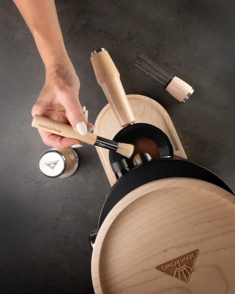 Overhead view of a hand brushing the portafilter on the maple Mahlkönig dosing tray