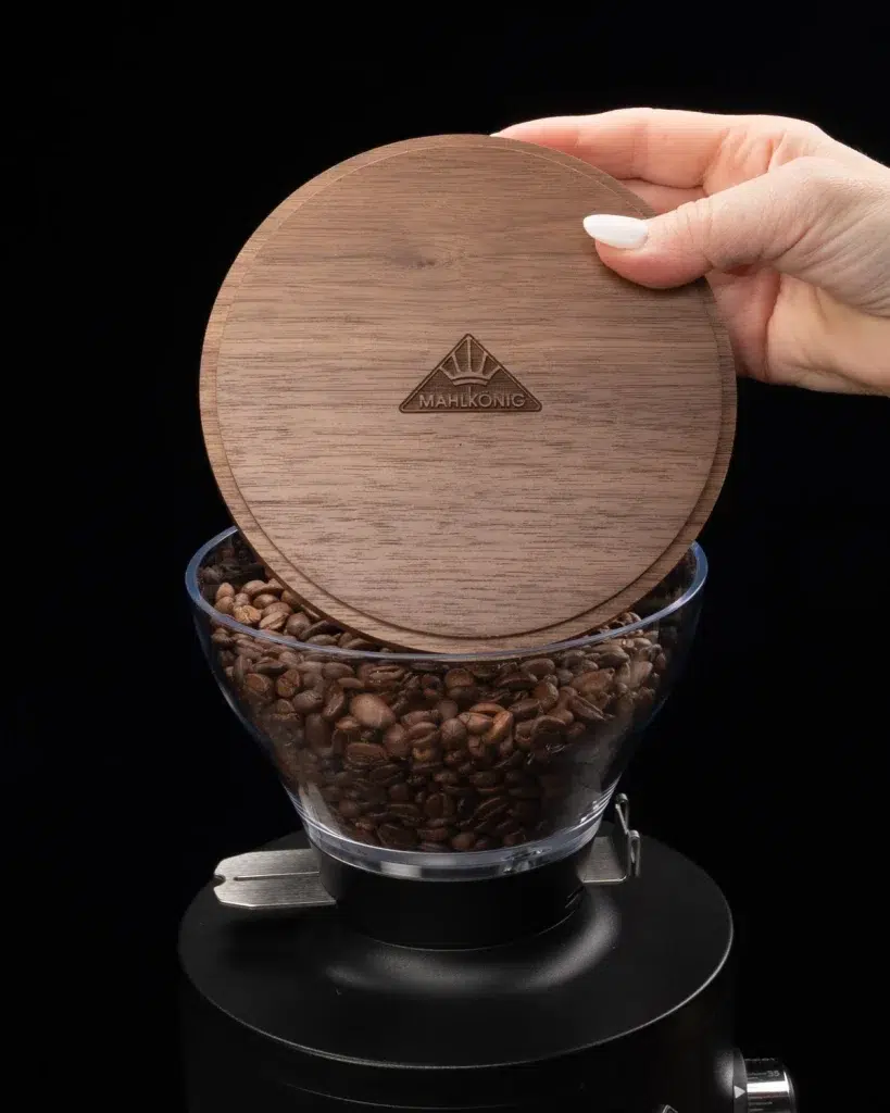 Hand lifting the engraved walnut Mahlkönig hopper lid off the glass bean hopper