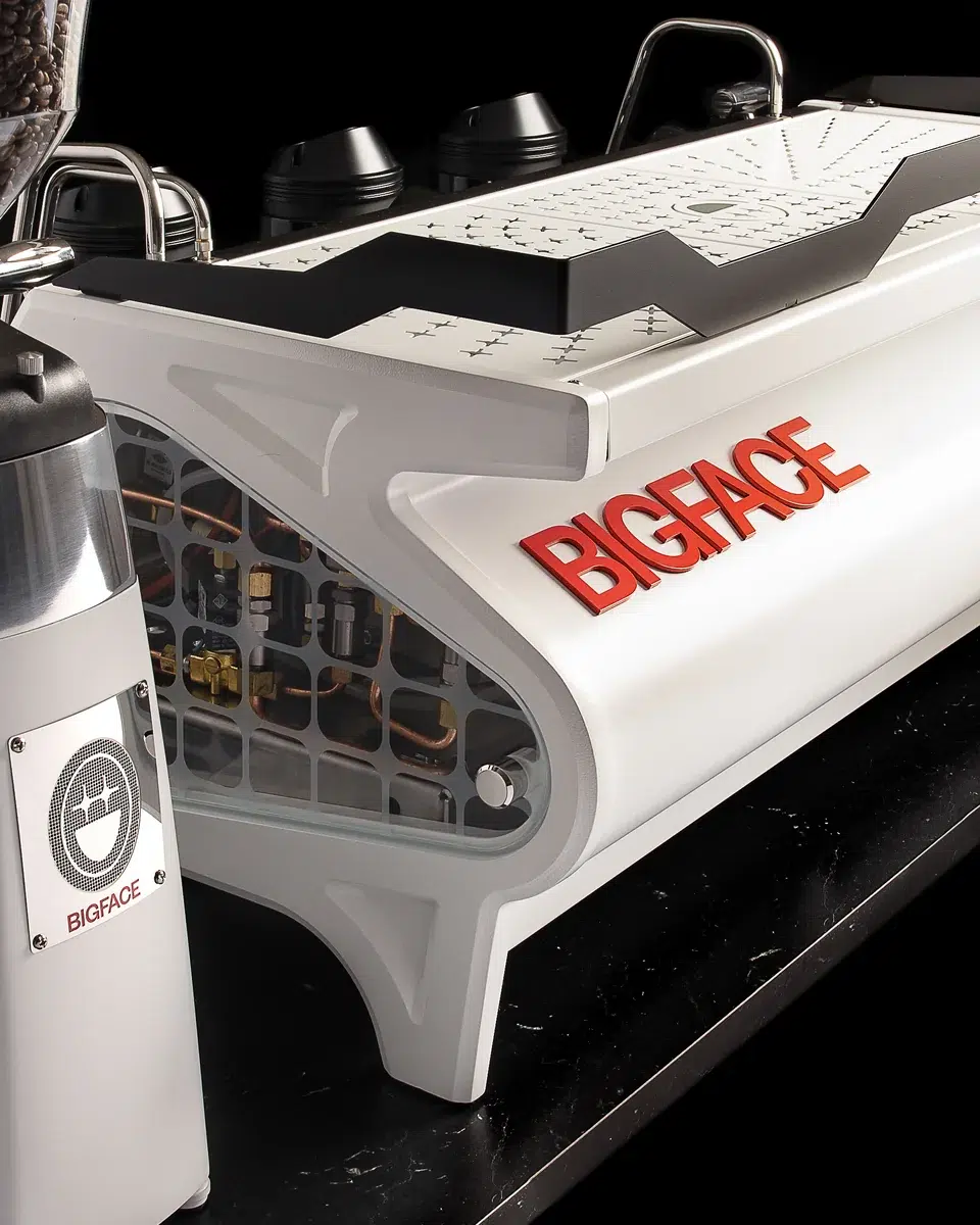 Glass side panel on the custom BIGFACE La Marzocco Strada showing the internal plumbing through the etched grid, with the red BIGFACE logo on the white body